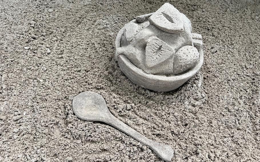 A sand sculpture of a bowl of strawberries and cream and a spoon.