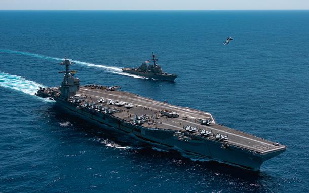 An F/A-18F Super Hornet, attached to the "Blacklions" of Strike Fighter Squadron (VFA) 213 and a F/A-18E Super Hornet, attached to the "Golden Warriors" of Strike Fighter Squadron (VFA) 87 fly over the world's largest aircraft carrier, USS Gerald R. Ford (CVN 78), the Arleigh Burke-class guided-missile destroyer USS Mahan (DDG 72), April 11, 2025. The Gerald R. Ford Carrier Strike Group is underway in the Atlantic Ocean completing integrated naval warfighting training. Composite Training Unit Exercise (COMPTUEX) is the Joint Force’s most complex integrated training event and prepares naval task forces for sustained high-end Joint and combined combat. Integrated naval training provides America’s civilian leaders and commanders highly-capable forces that deter adversaries, underpin American security and economic prosperity, and reassure Allies and partners. (U.S. Navy photo by Mass Communication Specialist 2nd Class Maxwell Orlosky