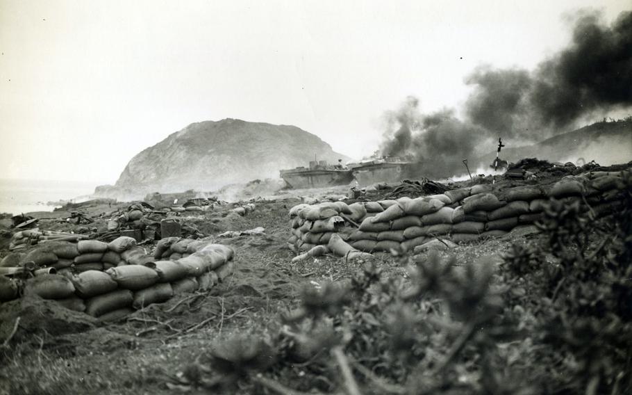 Military vehicles burn on an island during World War II.