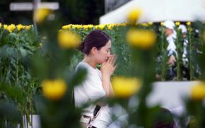 A woman holds her hands together beneath her chin as she bows her head in front of a memorial.