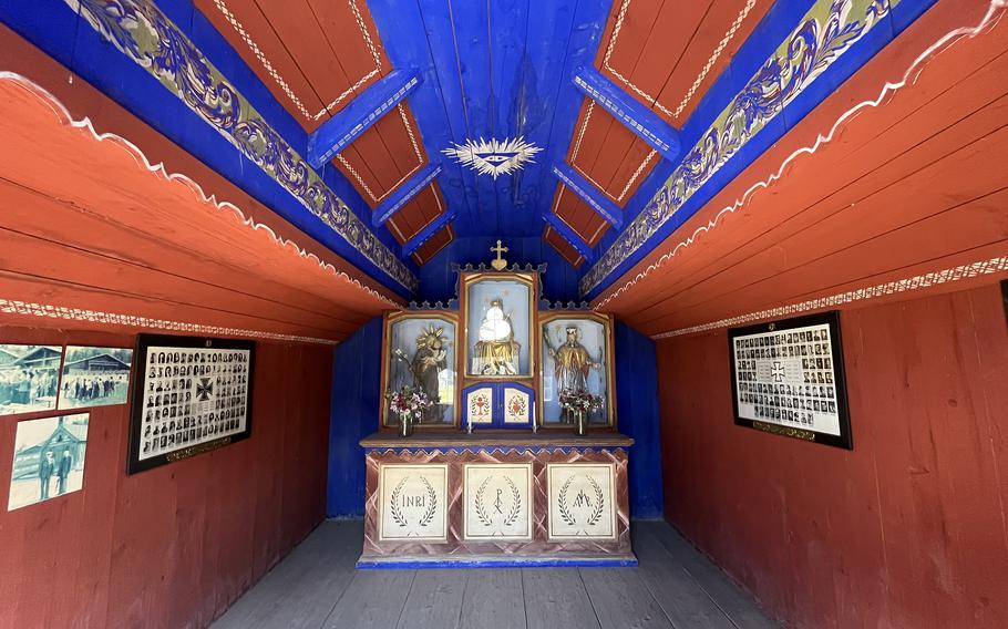 Interior of a small chapel with vibrant blue ceiling and red walls, featuring religious paintings, photographs of people arranged on the walls, and an altar with crosses and religious imagery.
