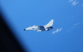 A military fighter aircraft flies against a bright blue sky with scattered white clouds. 