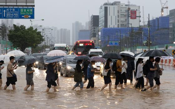 Pedestrians cross a flooded road at a junction in Gimpo, South Korea, on Aug. 9. MUST CREDIT: Bloomberg photo by SeongJoon Cho.