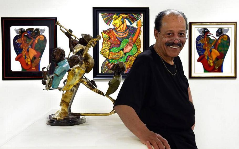 Ed Dwight in 2016, with his bronze sculpture on display at the American Jazz Museum. Behind Dwight are the paintings of Charles Biggs.