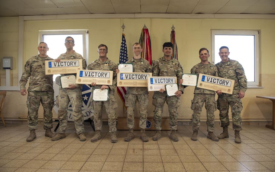 A squad of soldiers holds placards reading “Victory” indoors.