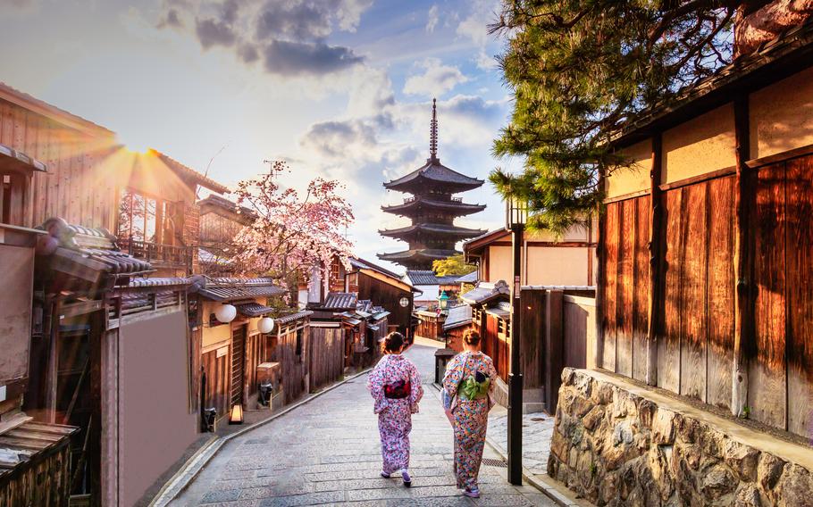 Visitors wander down a narrow street in the Higashiyama District neighborhood of Kyoto, Japan. Yasaka Pagoda is visible in the background.