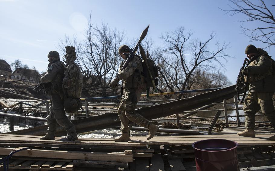 Ukrainian forces with rocket-propelled grenades cross under a damaged bridge in Irpin on March 12. 