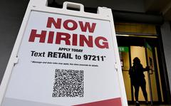 A woman walks past a "Now Hiring" sign in front of a store on January 13, 2022 in Arlington, Va. 
