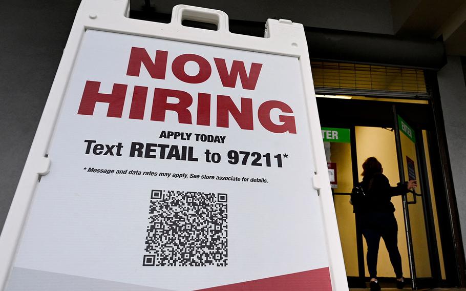 A woman walks past a “Now Hiring” sign in front of a store on January 13, 2022, in Arlington, Va. 