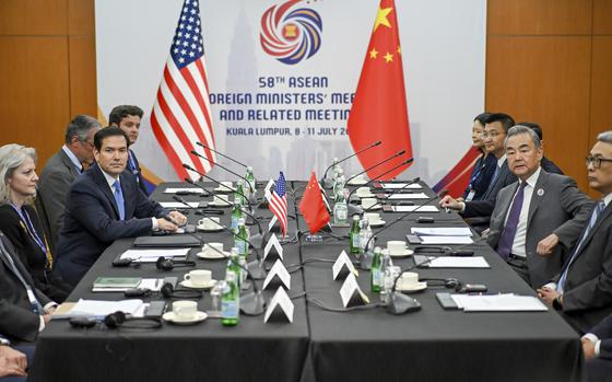 American and Chinese officials sit at microphones on opposite sides of a conference tables, with small U.S. and China flags on the middle of the table and larger flags behind them.