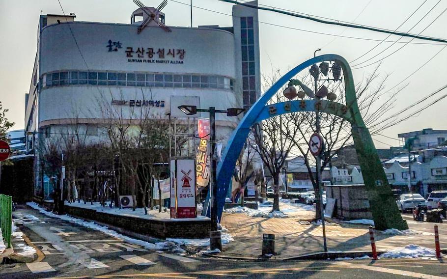A blue and green archway spans over the sidewalk entrance in front of a large building housing a South Korean market.
