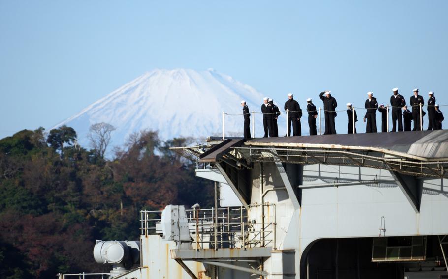 A snow-capped Mount Fuji towers in the distance as the aircraft carrier USS Ronald Reagan returns to Yokosuka Naval Base, Japan, Friday, Dec. 16, 2022. 