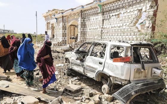 In this photo from February 16, 2022, women walk next to a destroyed house and the wreckage of a car following an explosion provoked by Al-Shabaab militants' during an attack on a police station on the outskirts of Mogadishu, Somalia. - Al-Shabaab militants launched simultaneous attacks on police stations around Somalia's capital Mogadishu overnight, killing two girls and wounding over a dozen people, security officials said Wednesday. (HASSAN ALI ELMI/AFP via Getty Images/TNS)