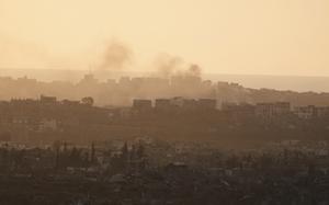 Smoke rises over a hazy city skyline with destroyed buildings in the foreground.