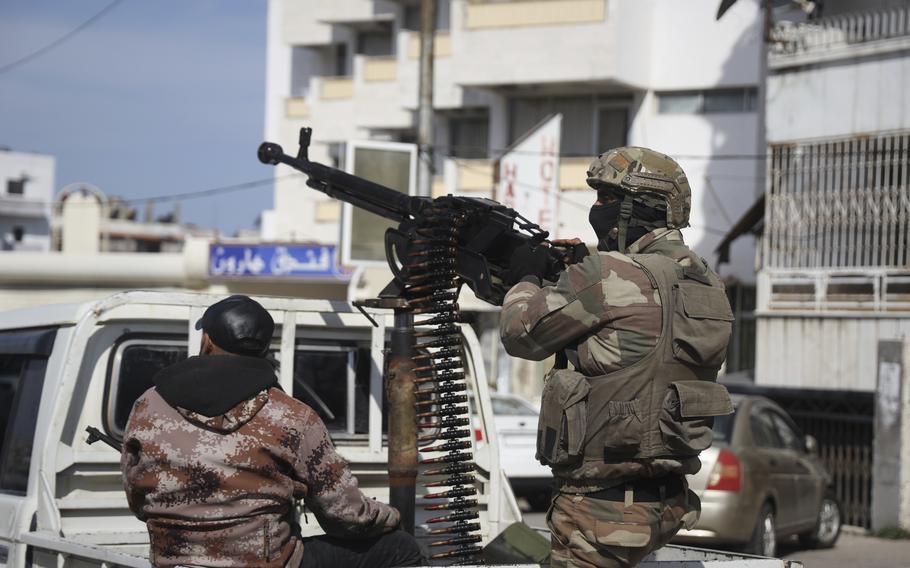 Two men in the back of a pickup truck, one in uniform holding a machine gun.