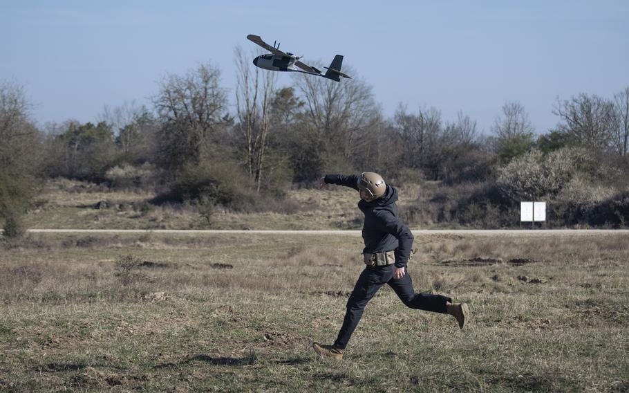A soldier hand-launches a handmade drone in a field.