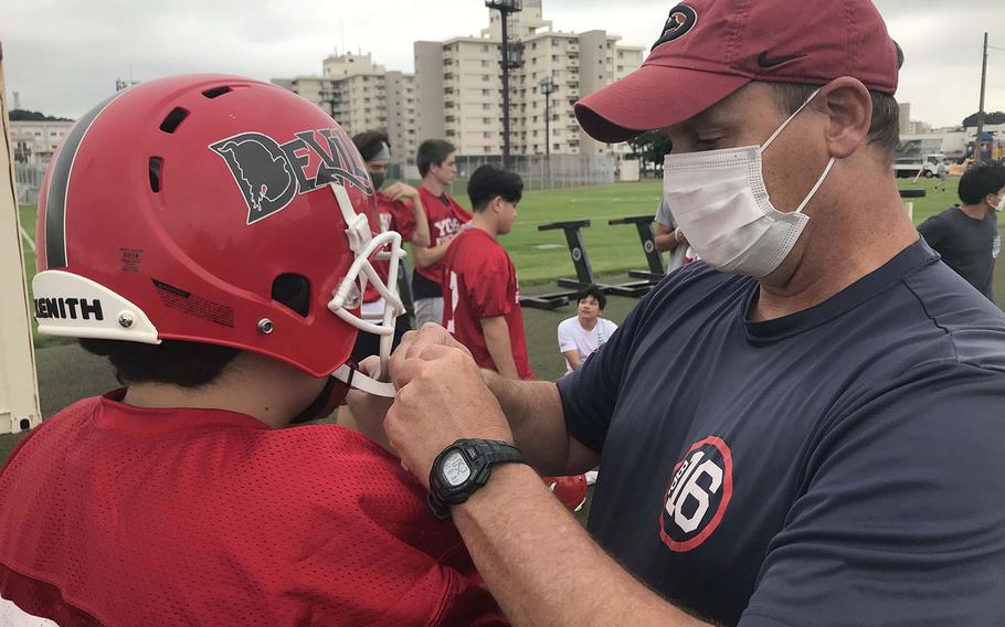 Nile C. Kinnick assistant coach Gary Wilson tends to the chinstrap on the helmet of Red Devils junior lineman Taiga Martin.