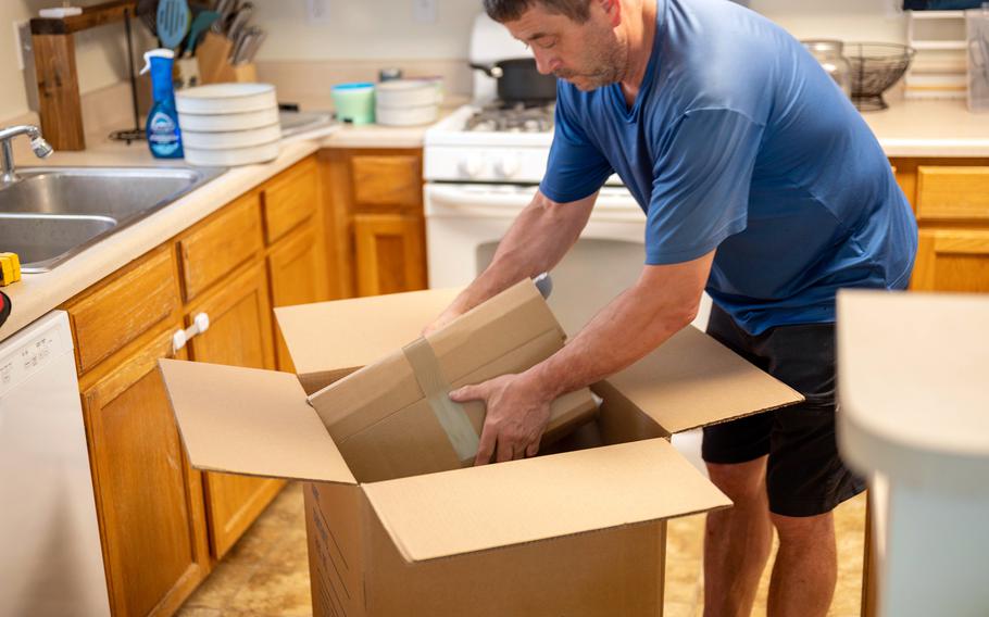 A man in a blue shirt packs a cardboard box.