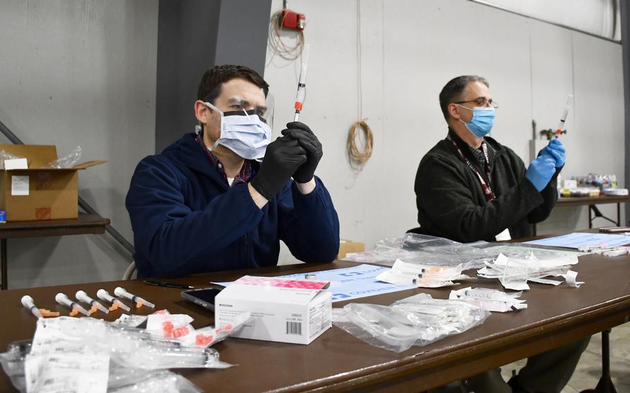 Pharmacists CJ Ludwig, front, and Chris Elizagaray, back, pull doses of the coronavirus vaccine from vials at a Department of Veterans Affairs vaccination clinic in Kalispell, Montana, on Tuesday, March 2, 2021.