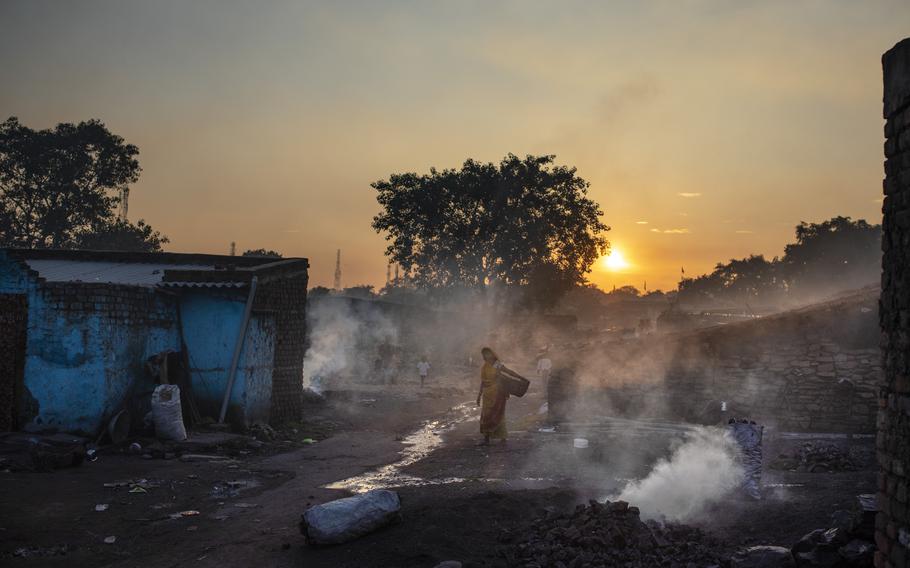 A woman walks past piles of coal burning after scavenging from an open-cast mine near Dhanbad, an eastern Indian city in Jharkhand state, Thursday, Sept. 23, 2021. On Saturday, India asked for a crucial last minute-change to the final agreement at crucial climate talks in Glasgow, calling for the “phase-down” not the “phase-out” of coal power.