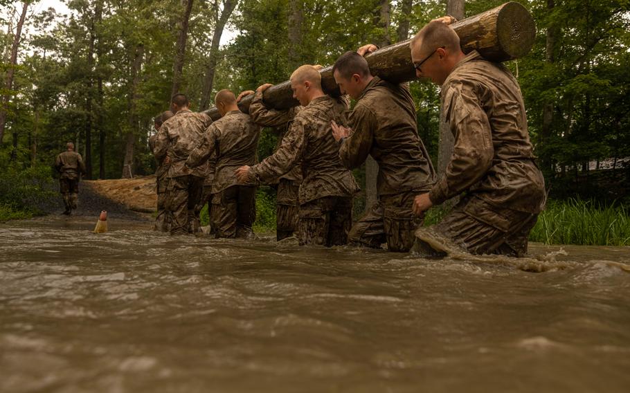 Marines carry a log through water.
