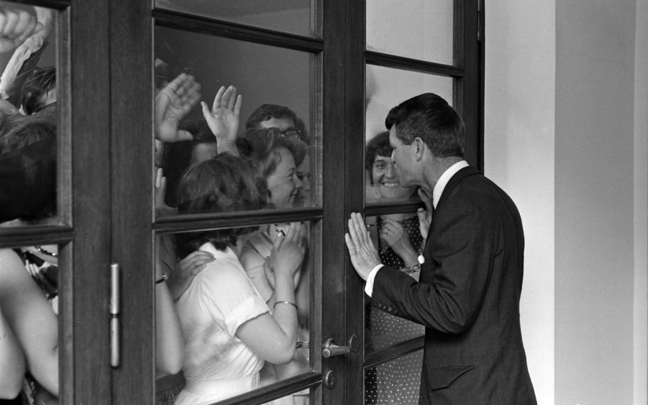 Admirers, mostly young women, near glass doors or windows with RFK on the other side.