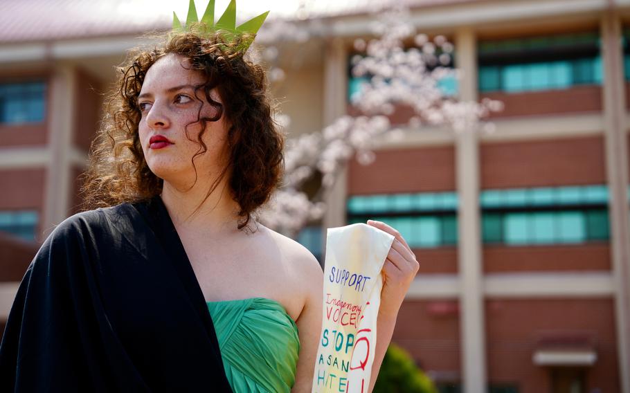 A high school student dressed as the Statue of Liberty holds up a sash with protest slogans on it.