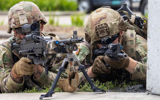 Two soldiers in combat gear lie on their stomachs and aim machine guns during an exercise.
