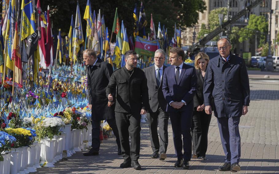 European leaders walk past a memorial of with yellow, white and blue flowers and Ukrainian flags.