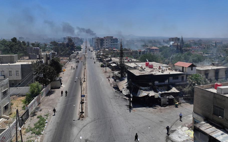 A view of a large street with buildings lining either side, some of which are smoking.