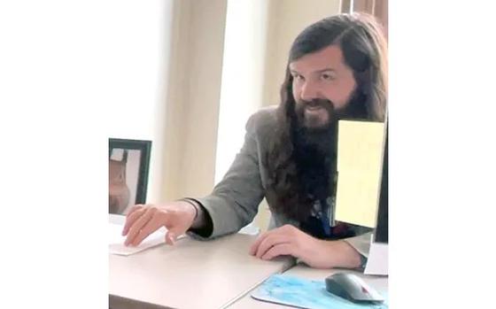 A man with long hair at a desk.