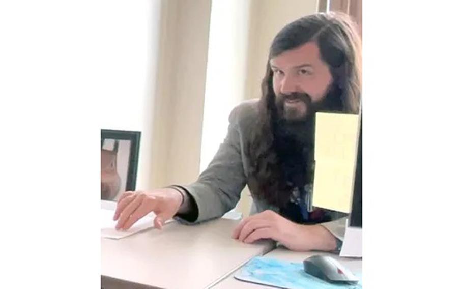 A man with long hair at a desk.