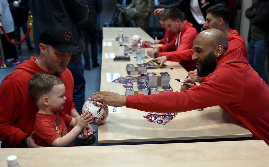 1. FC Kaiserslautern striker Terrence Boyd reaches to sign a ball from Brent, back, and Dex Habley on March 23, 2023, at the community center on Ramstein Air Base, Germany.