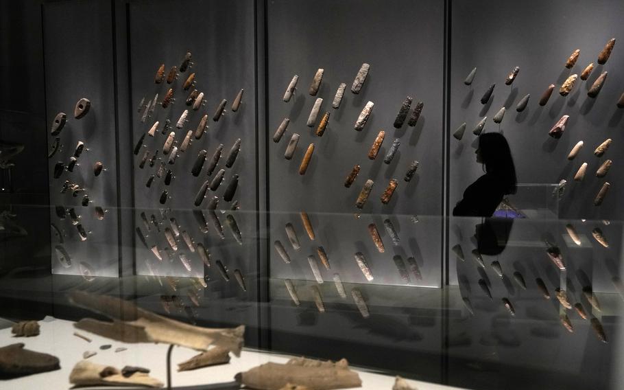 A member of staff poses next to a range of stone axe heads on display at the The World of Stonehenge’ exhibition at the British Museum in London, Monday, Feb. 14, 2022. The exhibition which displays objects and artifacts from the era of Stonehenge opens on Feb. 17 and runs until  July 17, 2022.