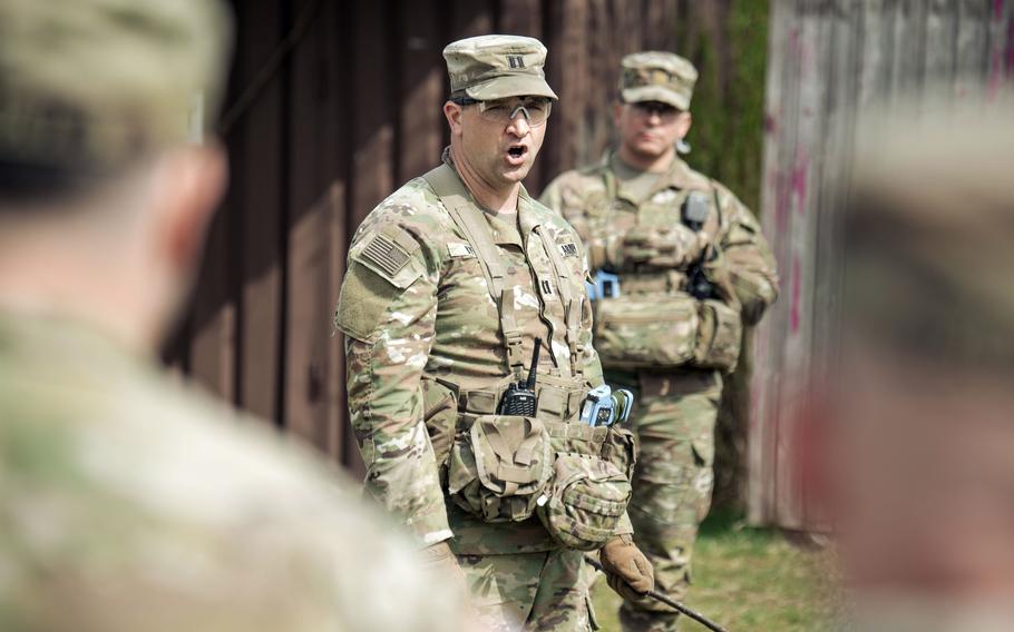 A US Army Captain speaks to a group of soldiers who standing around him.