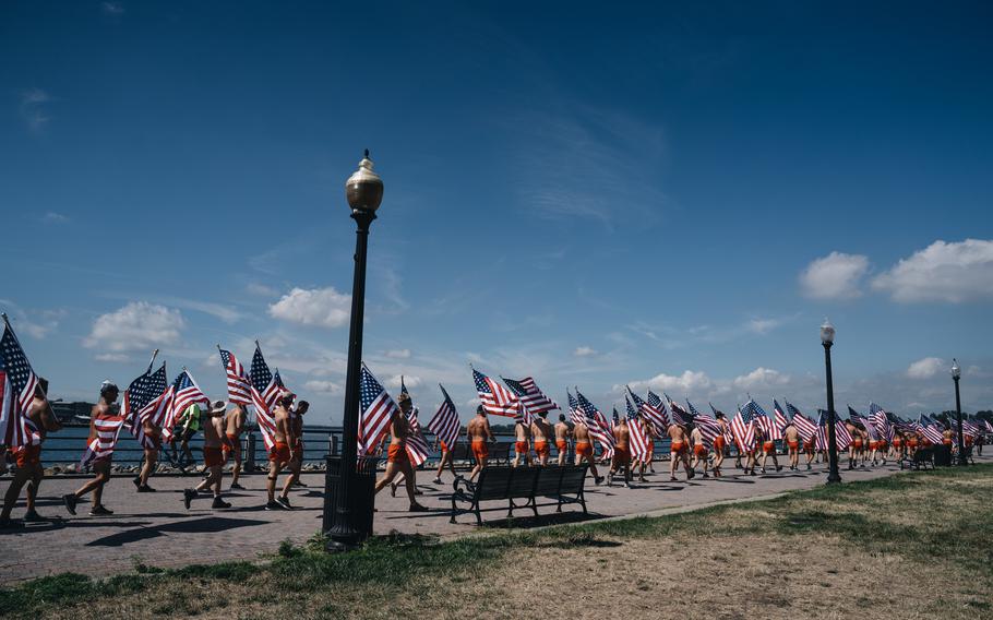 Participants in matching orange swim trunks for the 2022 NYC SEAL Swim jog with American flags from Battery Park to One World Trade Center.