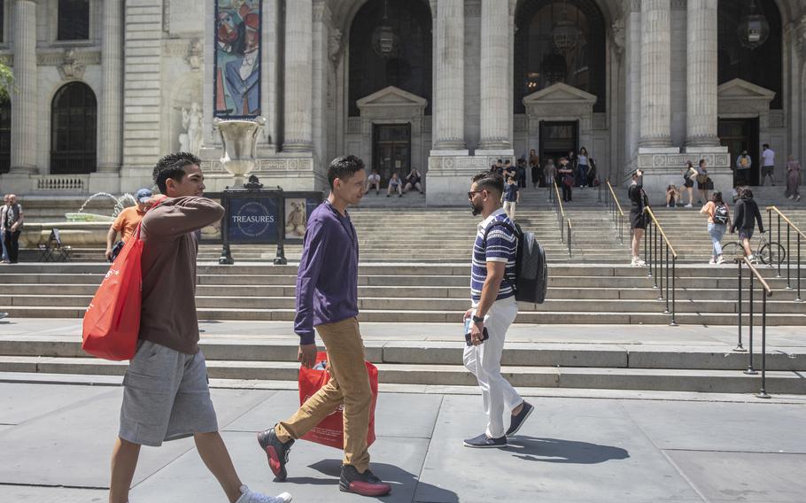 Antony Reyes, center, 23, with Brayan Cornieles, left, 19, on June 1, 2023, in New York City, carrying a bag of free clothing for himself and his nieces that he obtained at a pop-up donation center.