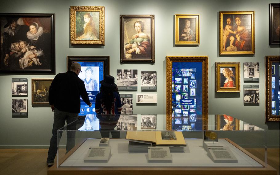 Two museum visitors look at a wall adorned with framed images.
