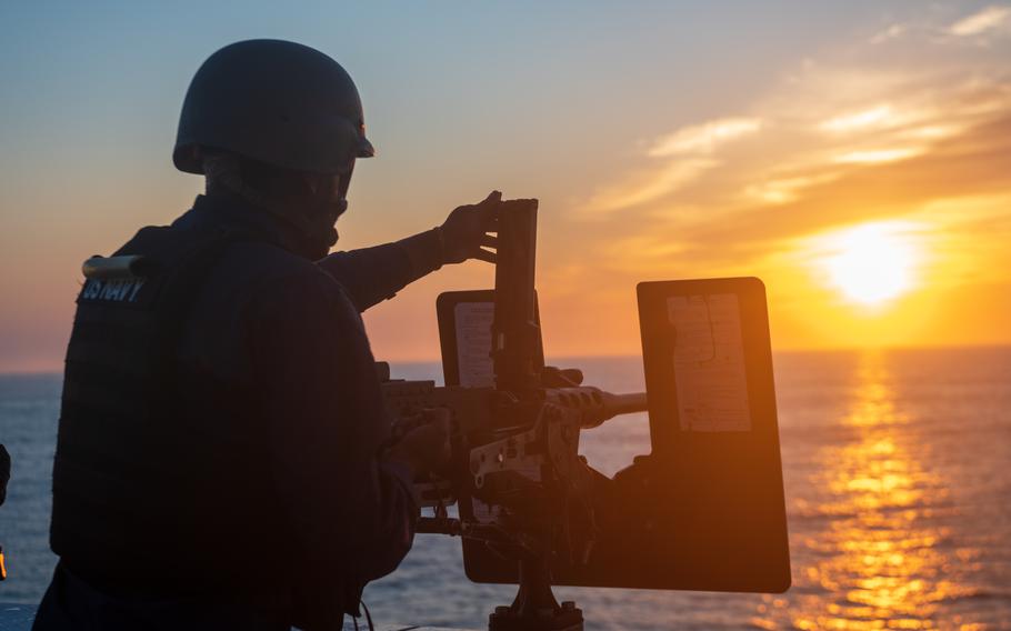 A sailor inspects a machine gun on a ship.