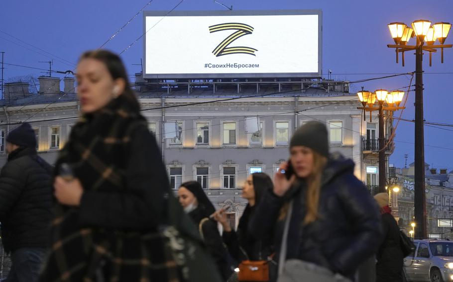 People walk past the letter Z, which has become a symbol of the Russian military, and a hashtag reading “We don’t abandon our own” on an advertisement screen in St. Petersburg, Russia, March 9, 2022. 