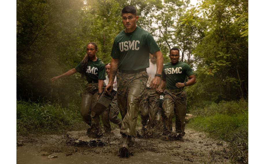 Marines carry ammo cans and walk through mud.