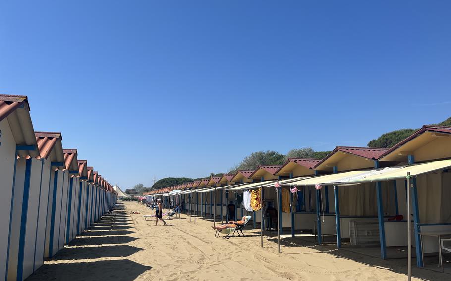 Beachgoers enjoy sunny weather in a row of cabanas.