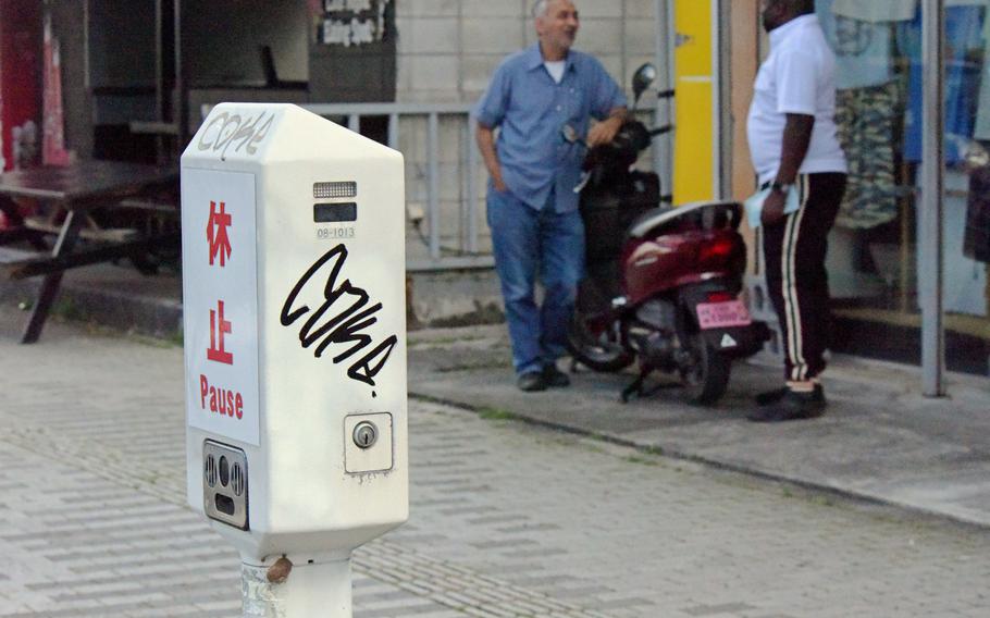 People chat near an out-of-service parking meter in Okinawa City, Okinawa, Tuesday, April 26, 2022. 