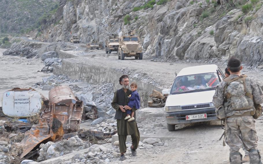 An Afghan man holds a child beside the remains of a tanker burned by insurgents along the Kunar River road. Soldiers securing the frequently hit site along the road on Aug. 1, 2010, stopped the man for questioning.
