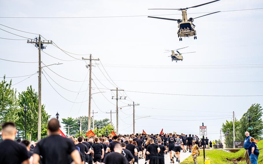 
Soldiers in black shirts and shorts running with helicopters flying overhead.