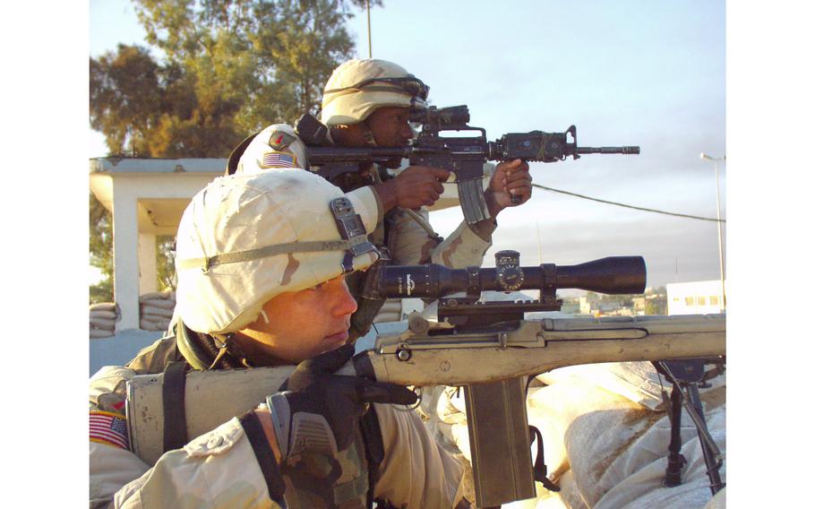 Spc. Greg McMeekan, 23, front, and Sgt. Melvin Davis, 32, scan the Bayji skyline from the roof of the mayor’s office, Nov. 25, 2004. The main street had been closed to Iraqi traffic during the day for the previous weeks during a violent uprising in the city so that U.S. supply convoys could safely pass. McMeekan and Davis were members of Company A of the 1st Battalion, 26th Infantry Regiment from Schweinfurt, Germany, but were then attached to Task Force 1-7.