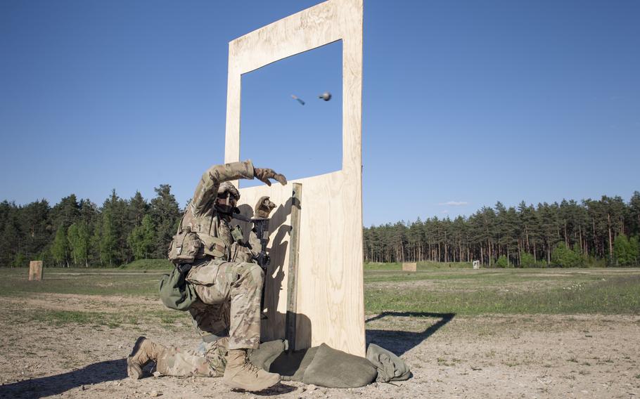 A dummy grenade flies through the air from the hand of a soldier kneeling behind a practice structure.