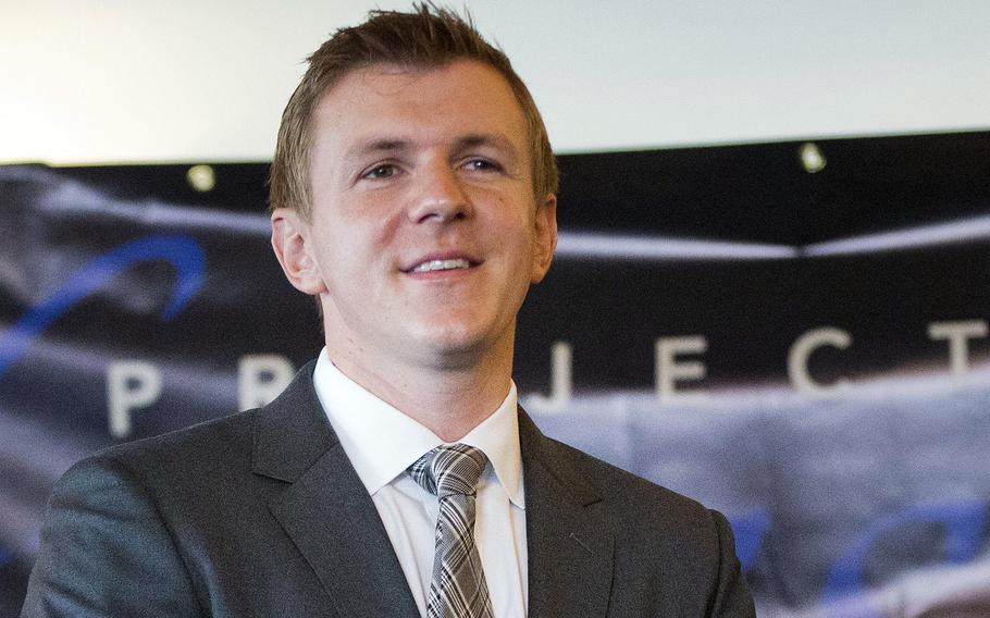 A man in a dark suit, seen from the chest up, stands on a stage in front of a banner reading “Project Veritas.”