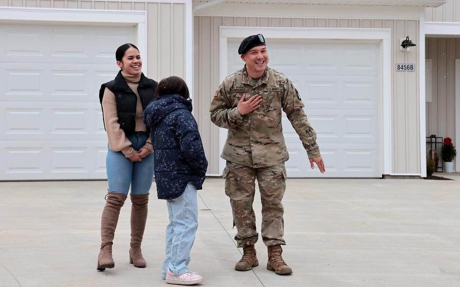 A soldier, his wife and their daughter standing in the driveway of some houses. 