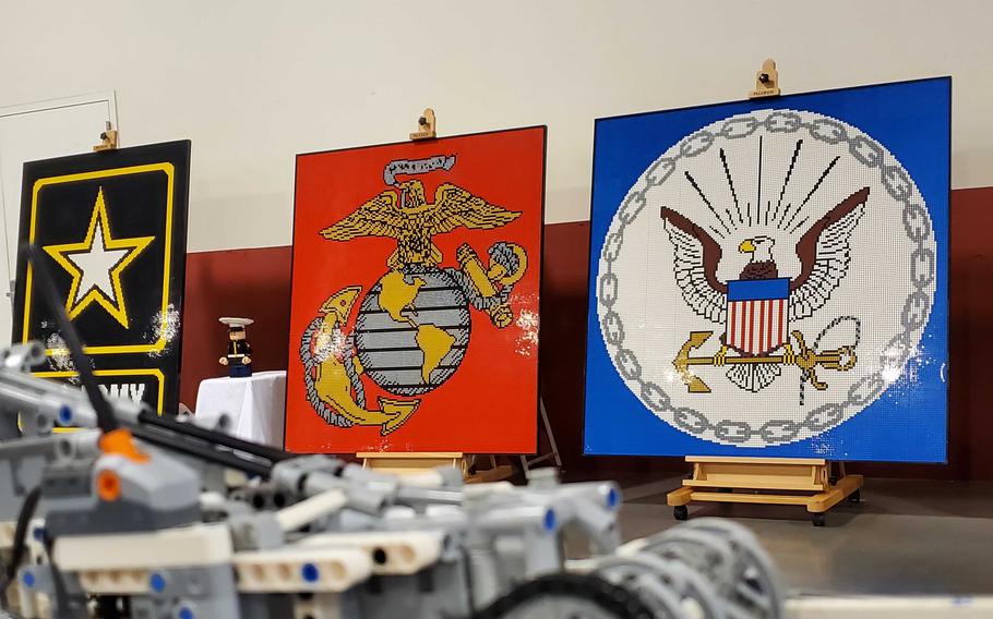 Three large LEGO mosaics int he shape of logos for the Army, Marine Corps and Navy rest on easels in front of a white and red wall.